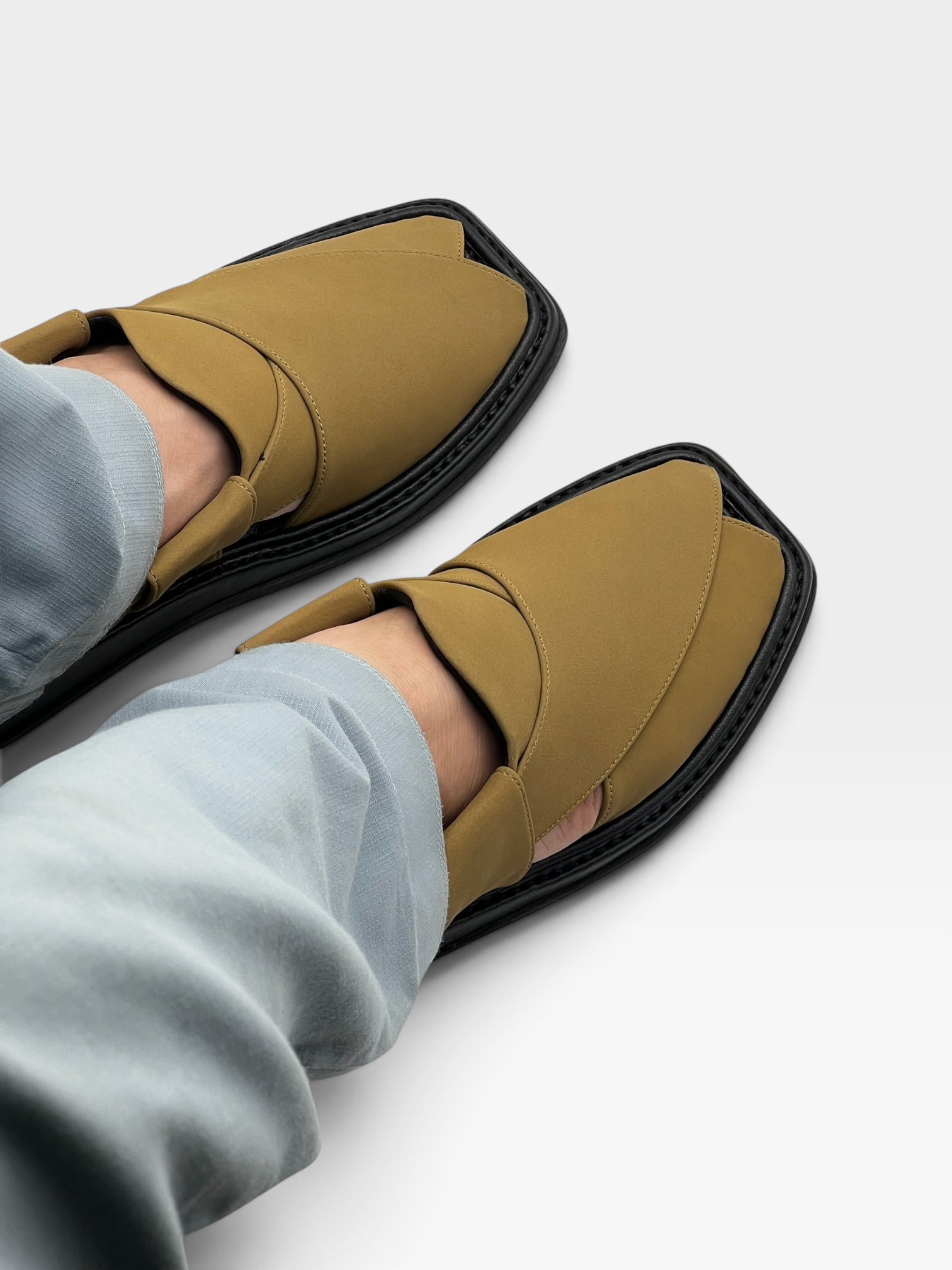 Pezaar Collection tan Peshawari chappal sandals with a black sole worn with light blue trousers on a white background